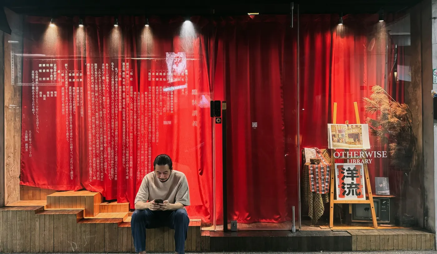 延平北路二段 33 號的店面:紅色布幔上印著〈臨床講義〉日文原文,門口有人坐在木階上看手機,櫥窗裡架著 OTHERWISE LIBRARY 的招牌和一幅大安醫院的畫