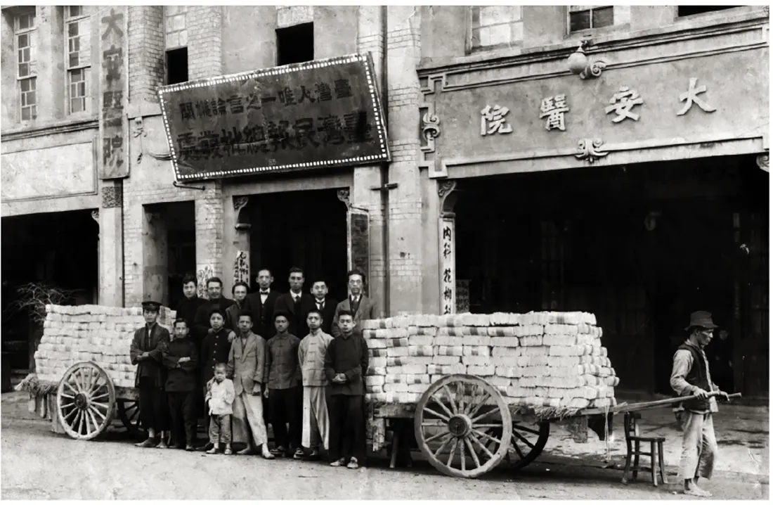 大安醫院門口,招牌寫著臺灣民報總批發處,十幾個人站在兩台堆滿報紙的板車之間